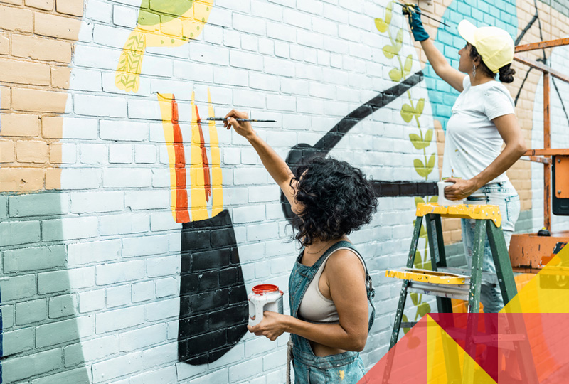 Photo of artists painting a mural on a brick building