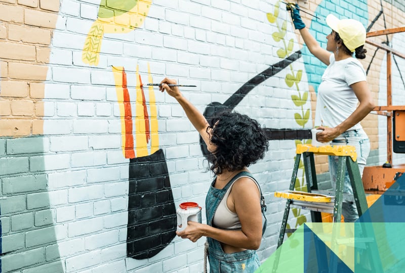Photo of artists painting a mural on a brick building